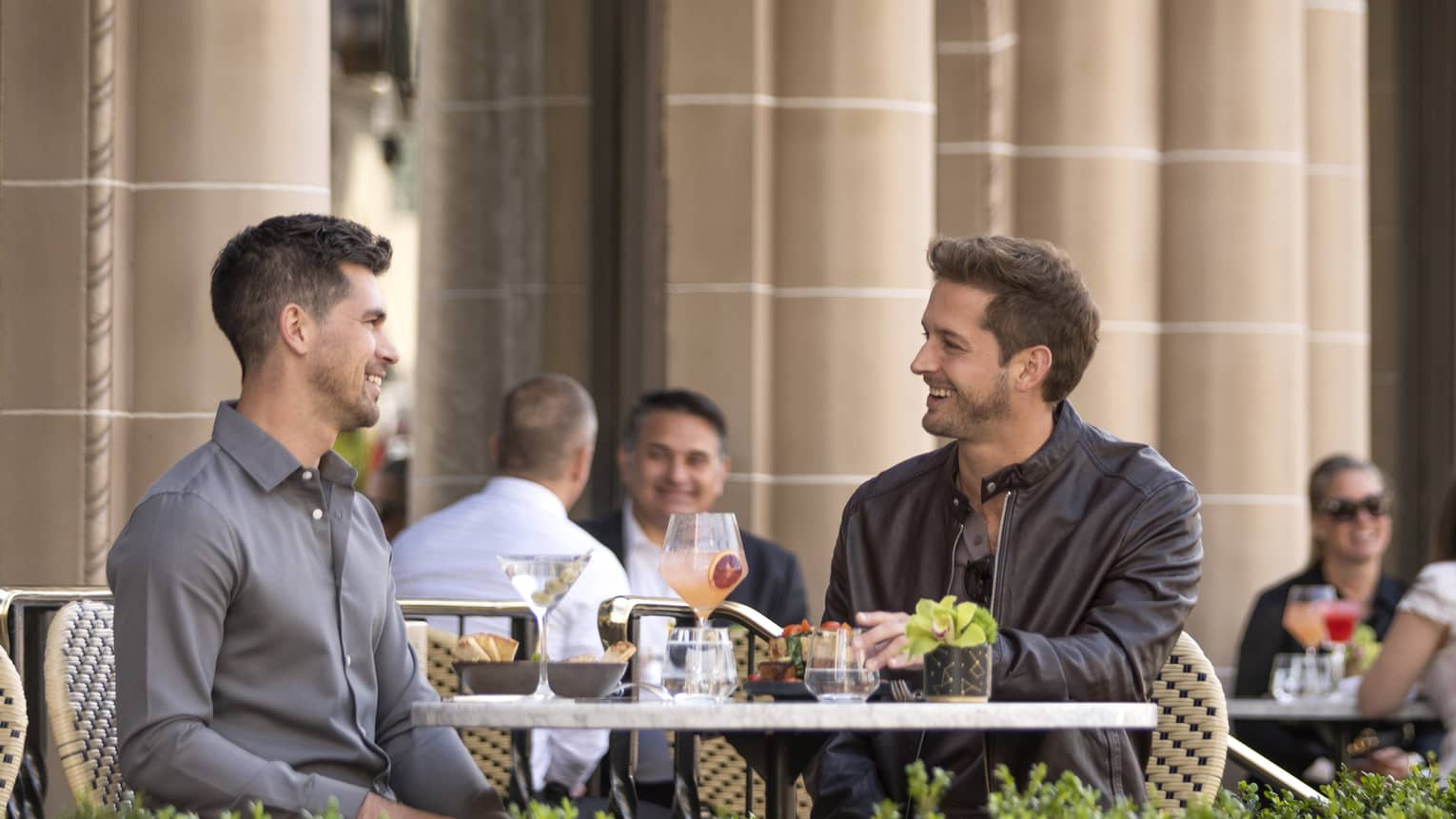 Two men eating at a patio outside.
