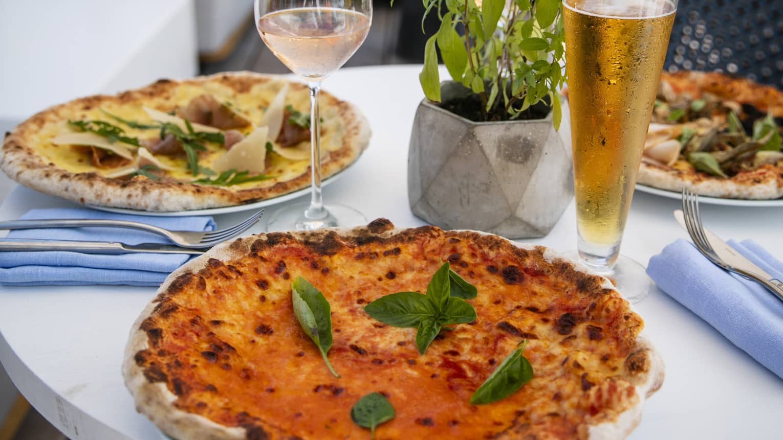 A table set with a glass of rose and a pilsner of beer with craft pizzas on it overlooking the beach at Four Seasons Maldives - Landa