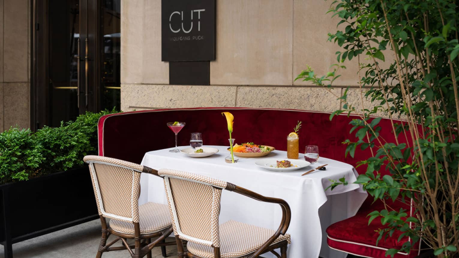 ,An outdoor table with two wooden chairs and a red velvet booth set with colorful food and beverages