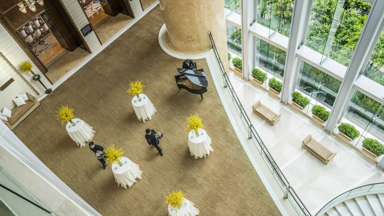 From above, a view of pre-function space set with five cocktail tables, each with yellow flowers. Two servers walk through the tables.