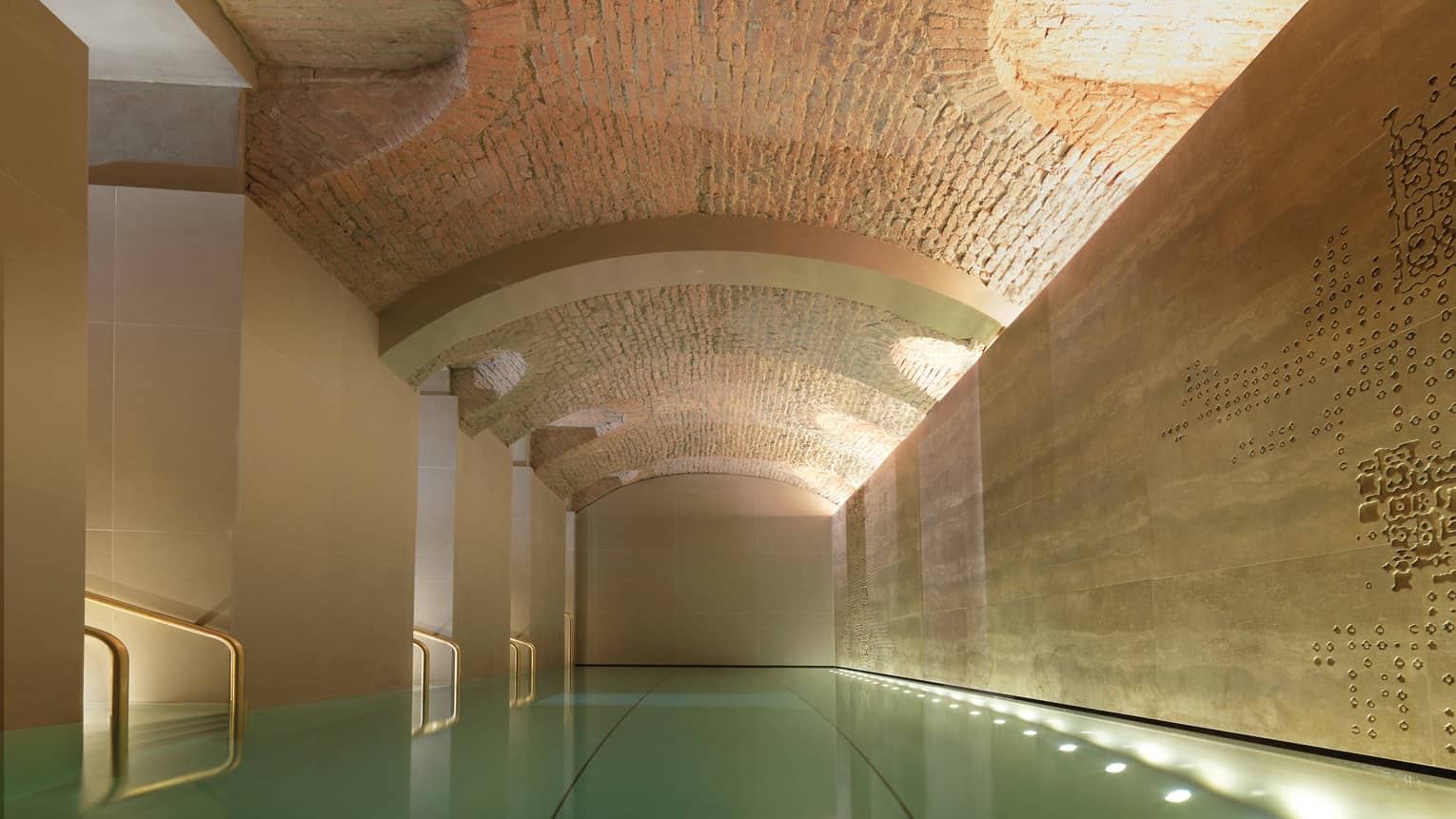 Indoor lap swimming pool with gold railings under curved stone ceiling