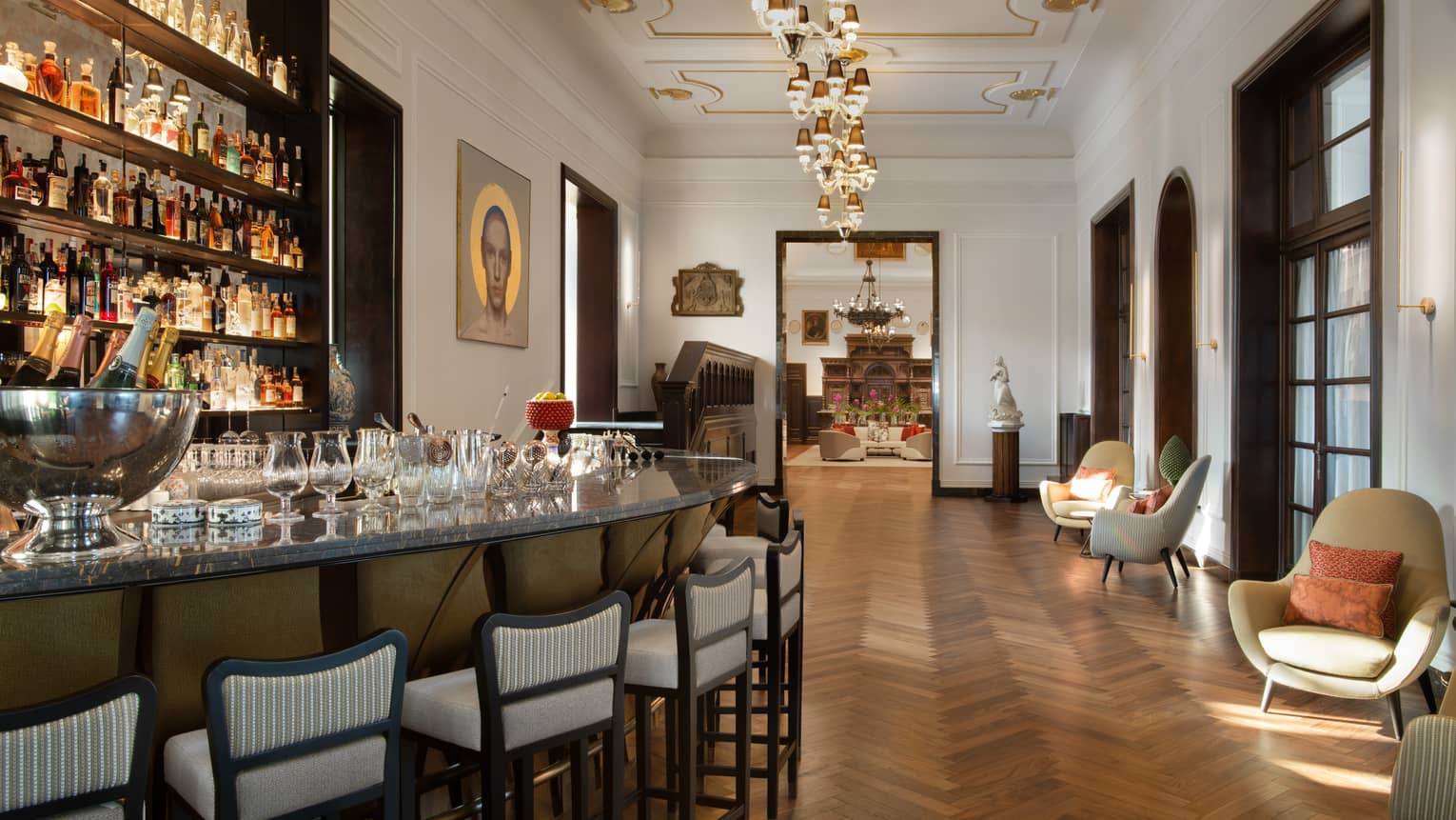 Indoor bar with parquet floors, curved bar with cushioned high-top chairs, wall of bottles