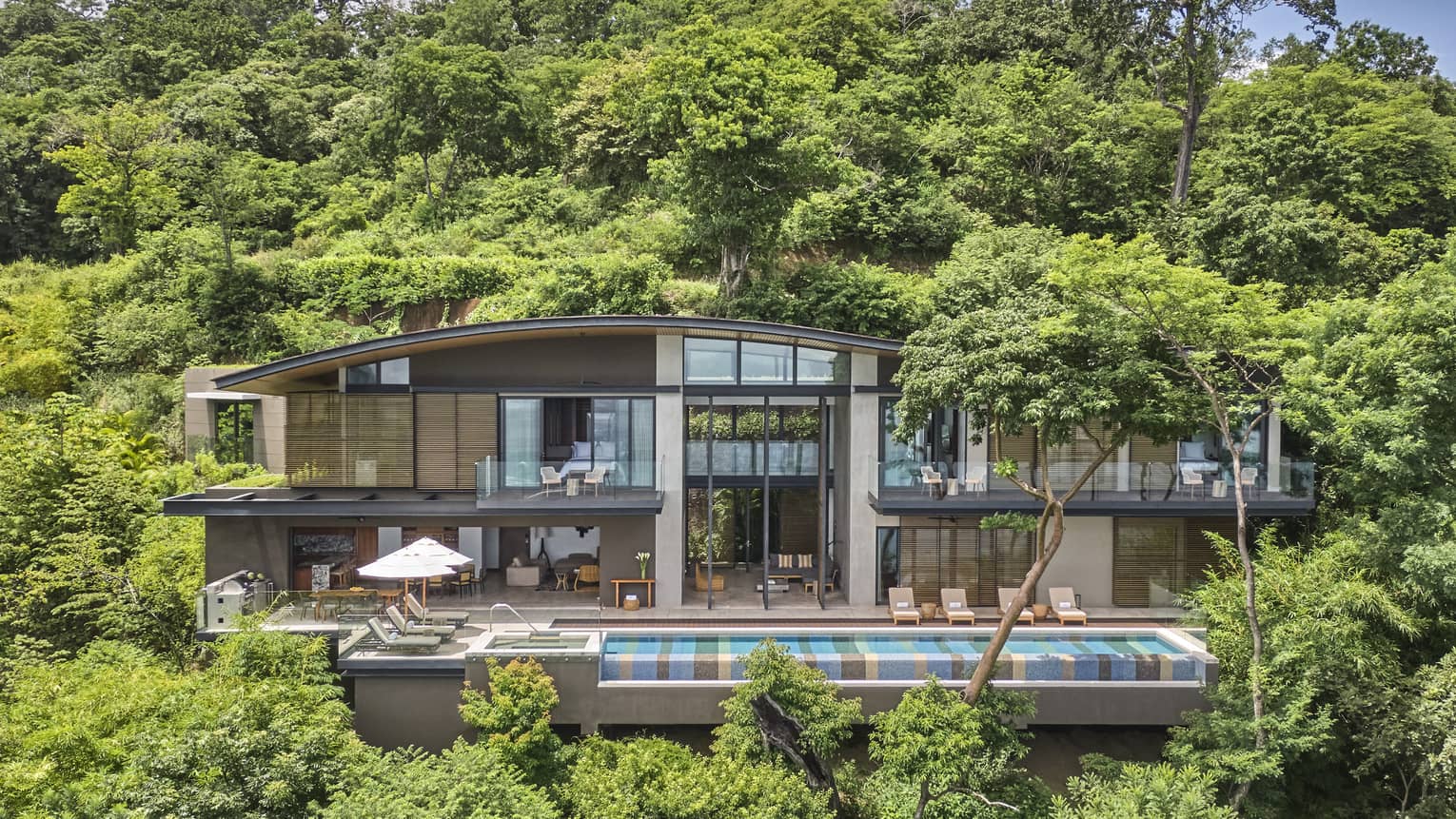 Exterior of private villa nestled in the trees with long rectangular pool