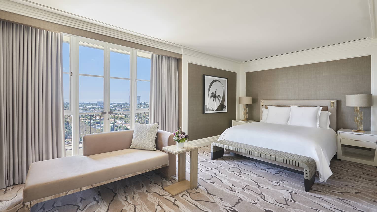 Bedroom with king bed, beige chaise, tan walls, glass French doors opening to Juliette balcony