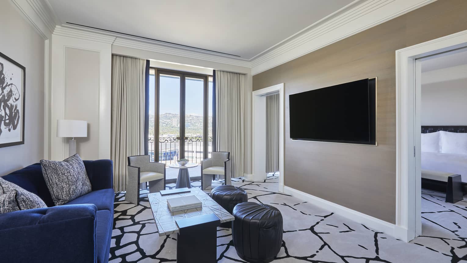Living room with royal blue sofa, black and white carpet, wall-mountain TV, and an entrance into bedroom