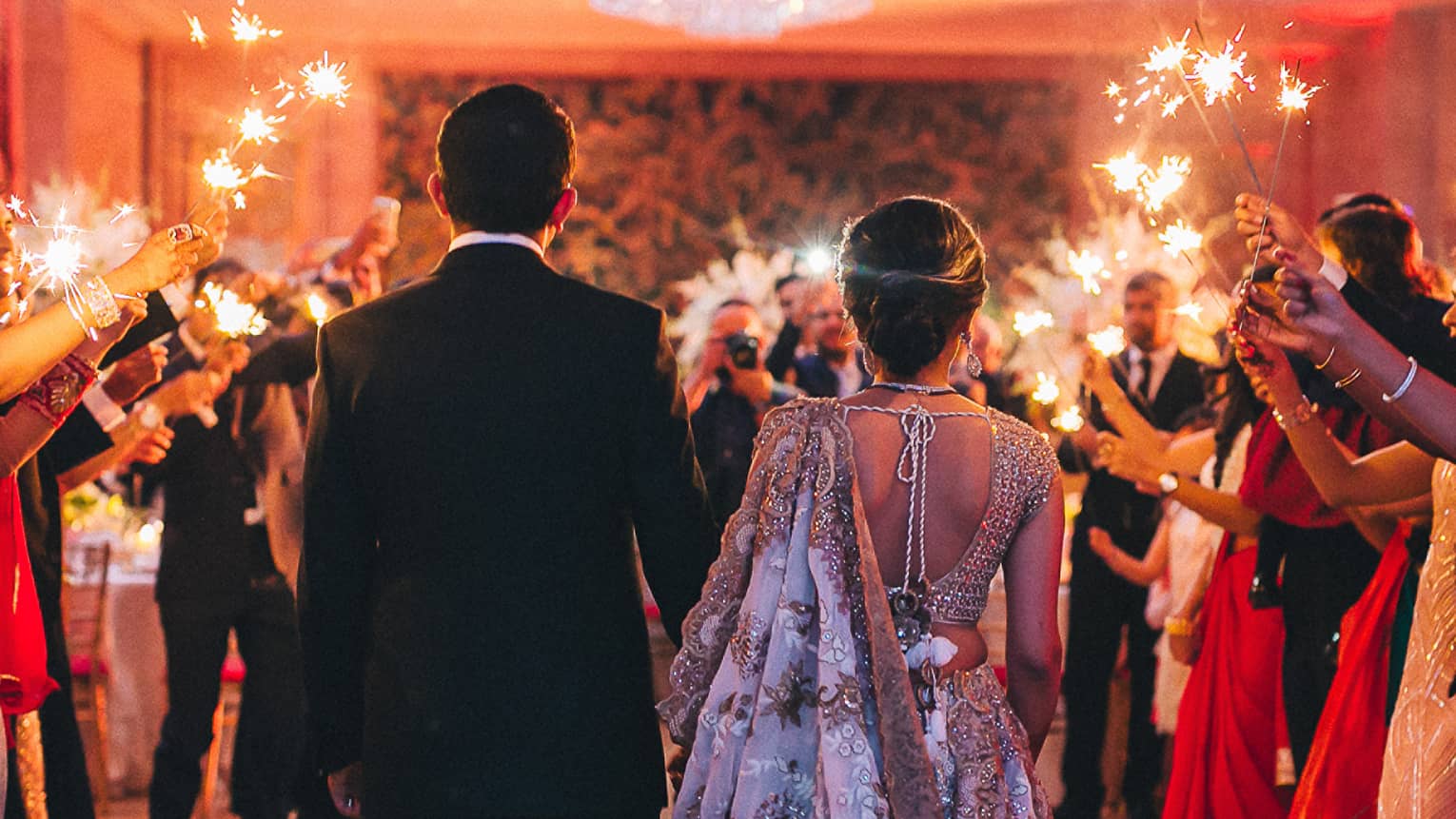 Back of bride and groom entering wedding reception as guests hold sparklers around them