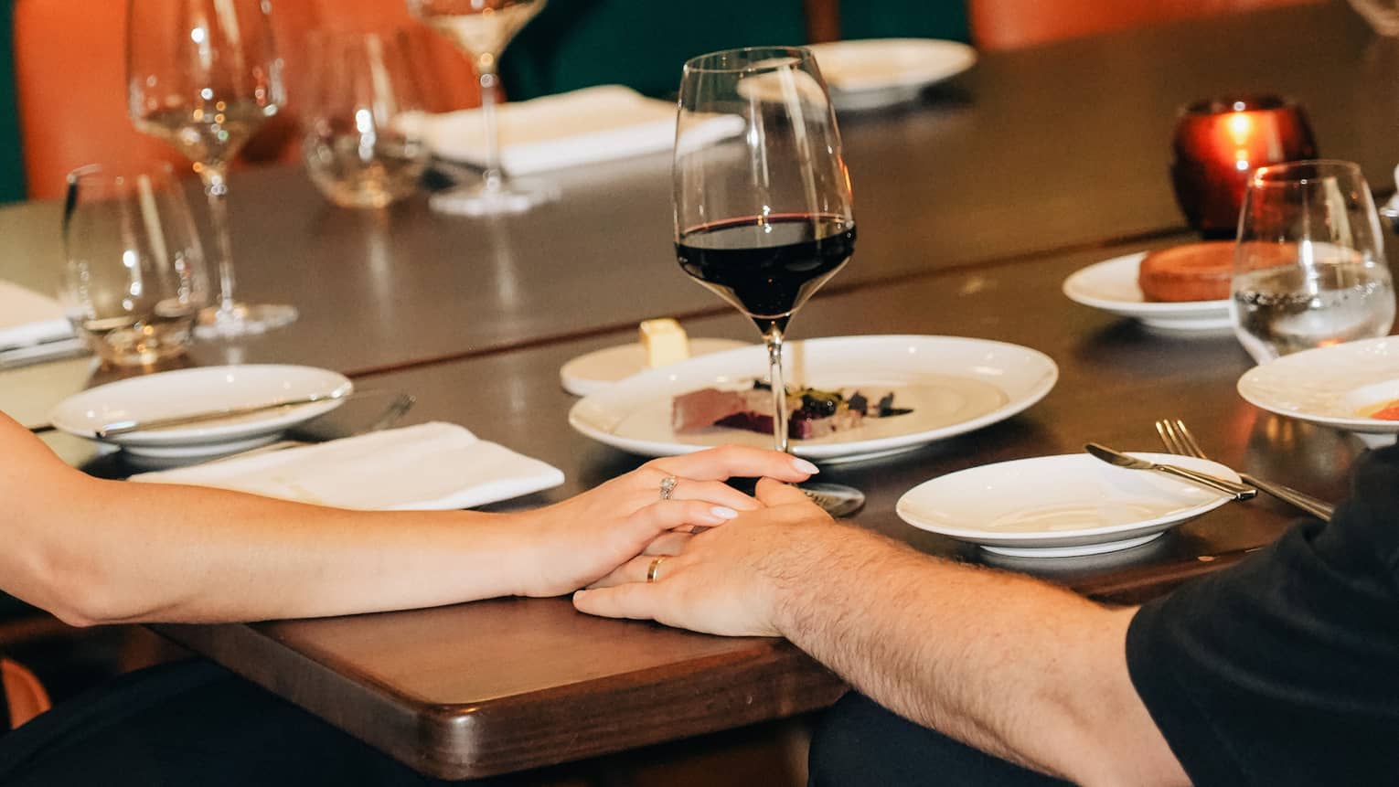 Two people hold their hands together on top of a restaurant dining table