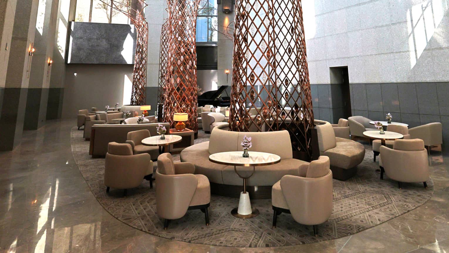Lounge set in the centre of a hotel lobby beneath towering two-storey ceilings with natural sunlight streaming through a large wall of paned windows