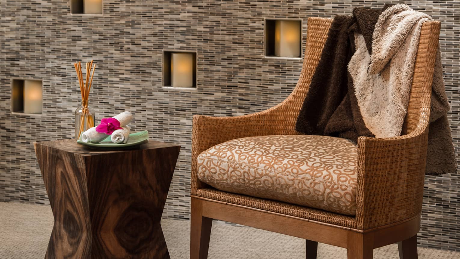 Blanket across back of wicker chair in front of wall with candles, beside wood table