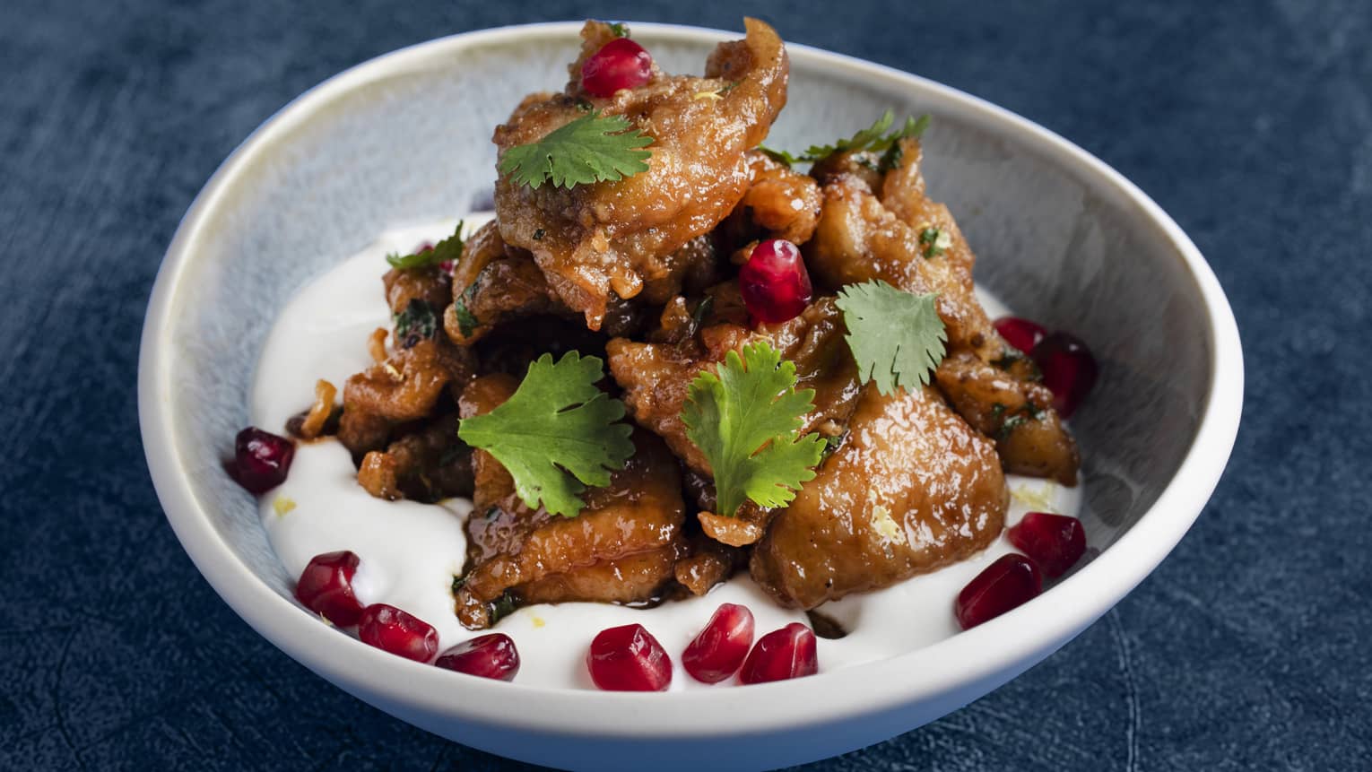 Crispy boneless chickens wings with coriander labneh sauce and pomegranate seeds in a white bowl