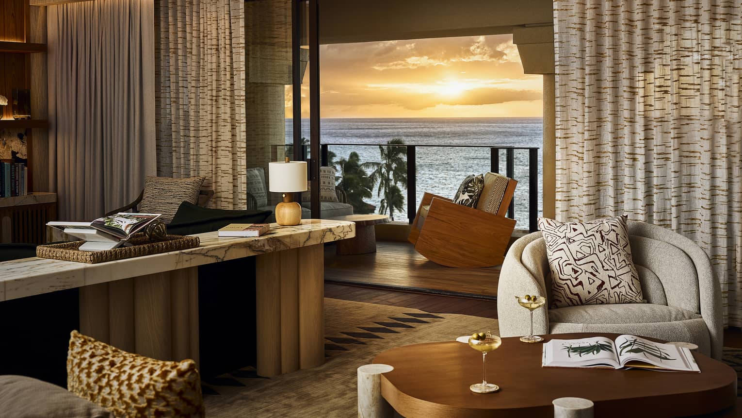 Living room opening to an ocean-view balcony with sunset view in luxury resort suite