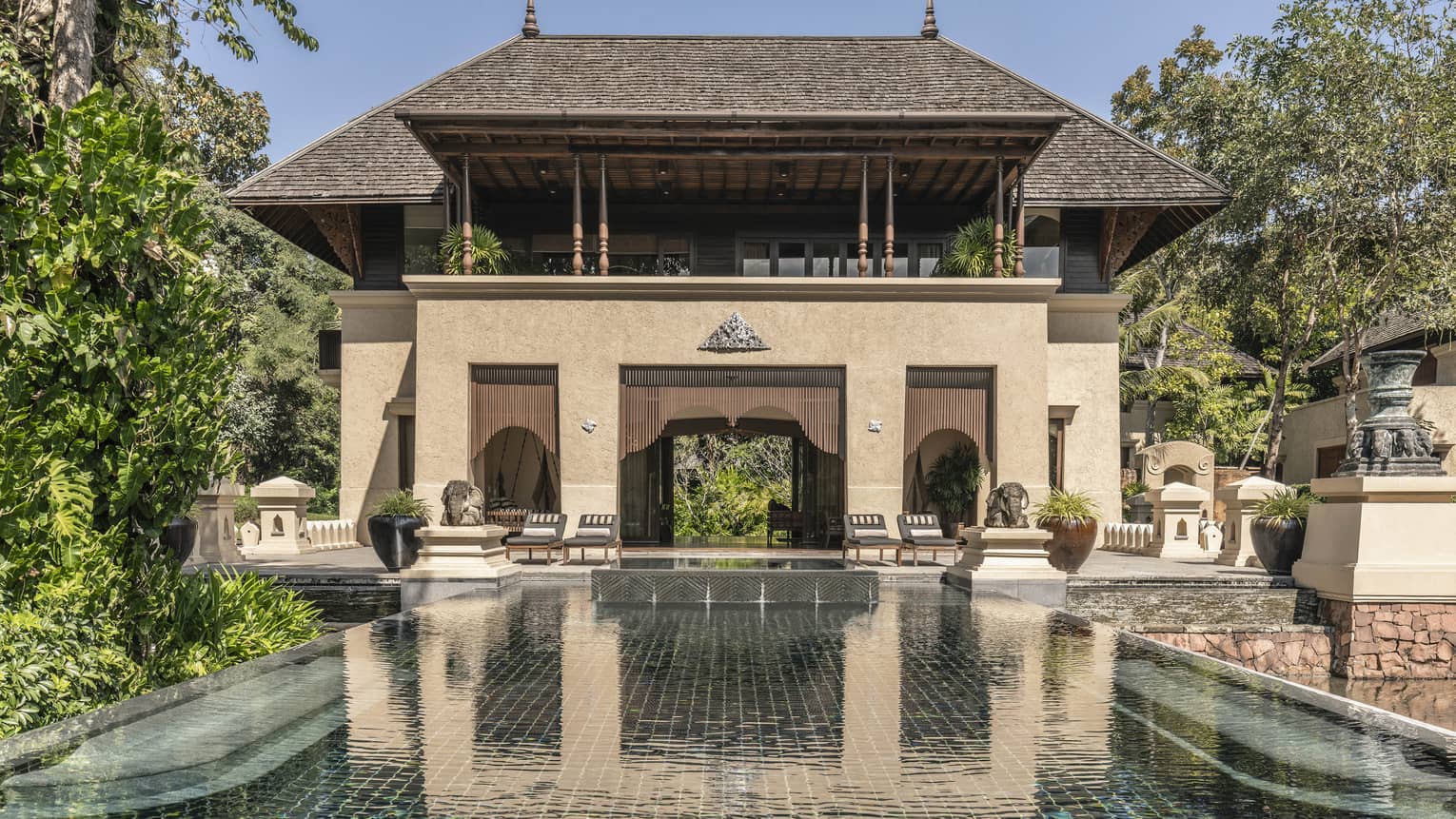 A large brown villa with a pool extending out from it.