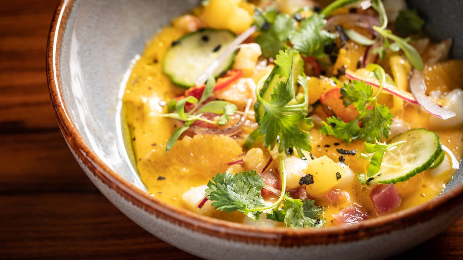 A bowl of yellow ceviche with scallops and shrimp garnished with citrus and cilantro.