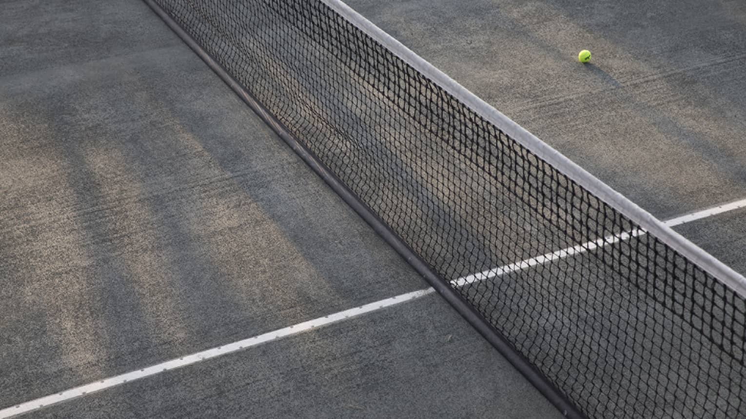 A lone tennis ball lies near the net on an empty court