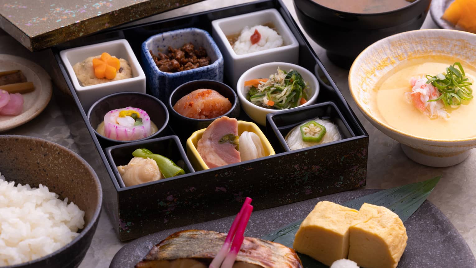 Traditional Japanese bento box breakfast with obanzai side dishes, tamagoyaki (Japanese rolled omelette), congee, steamed rice and miso soup