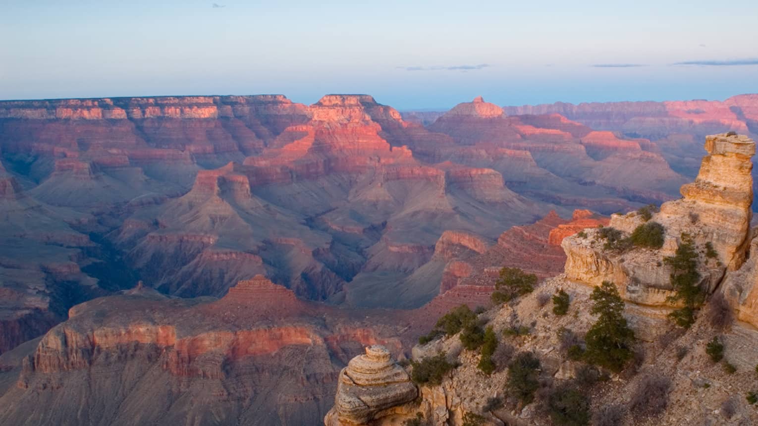 Sweeping view of Grand Canyon cliffs, canyon ridges, pink light from sunset