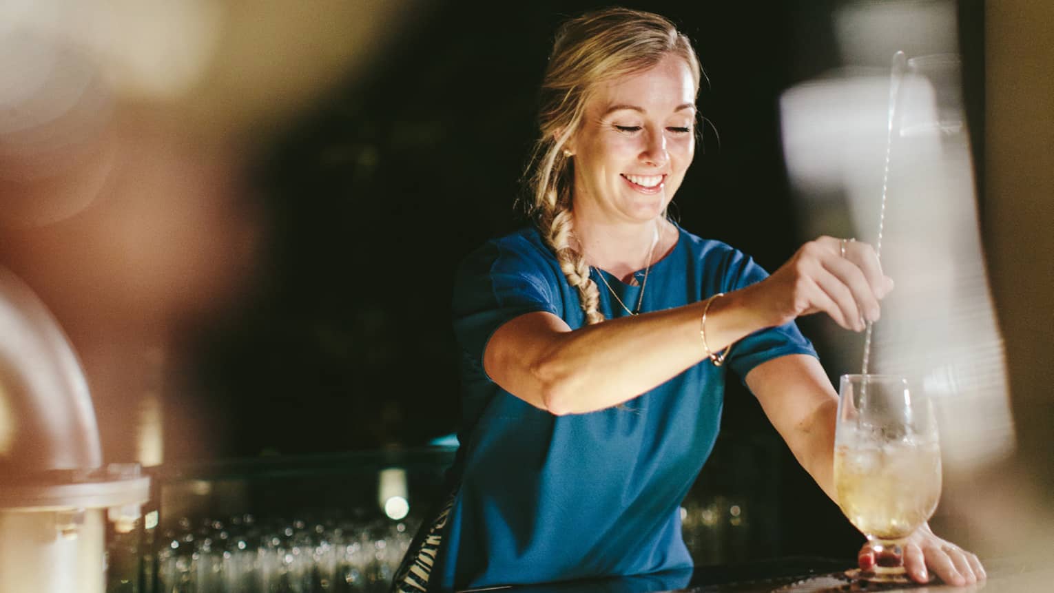 A mixologist puts together a drink at Lobby Lounge, Four Seasons Resort Maui at Wailea. She is mixing the drink and smiling.