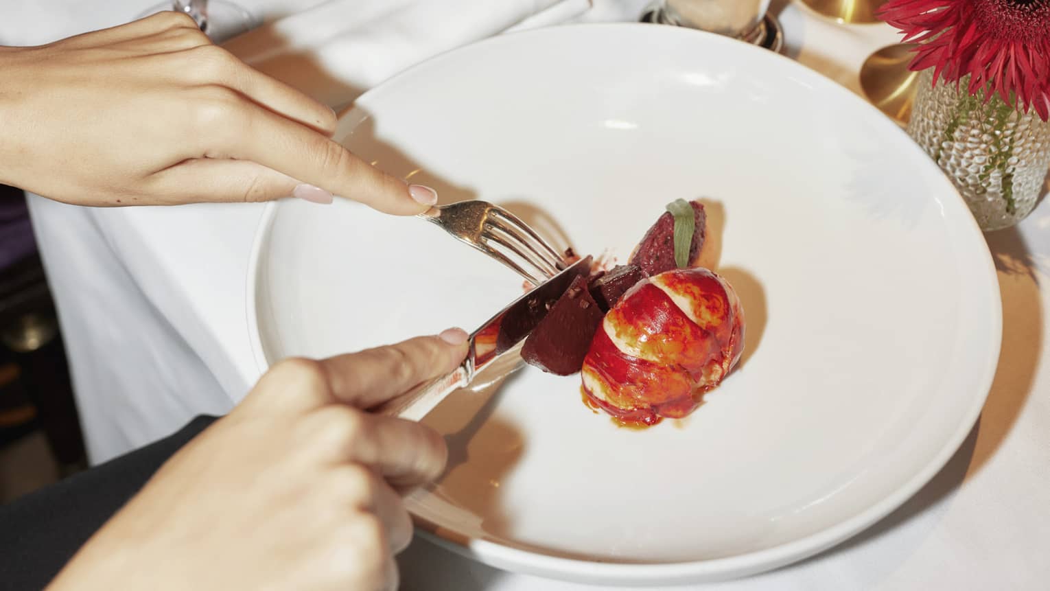Two people sit at white-cloth table, cutting into contemporary dish on large white plate