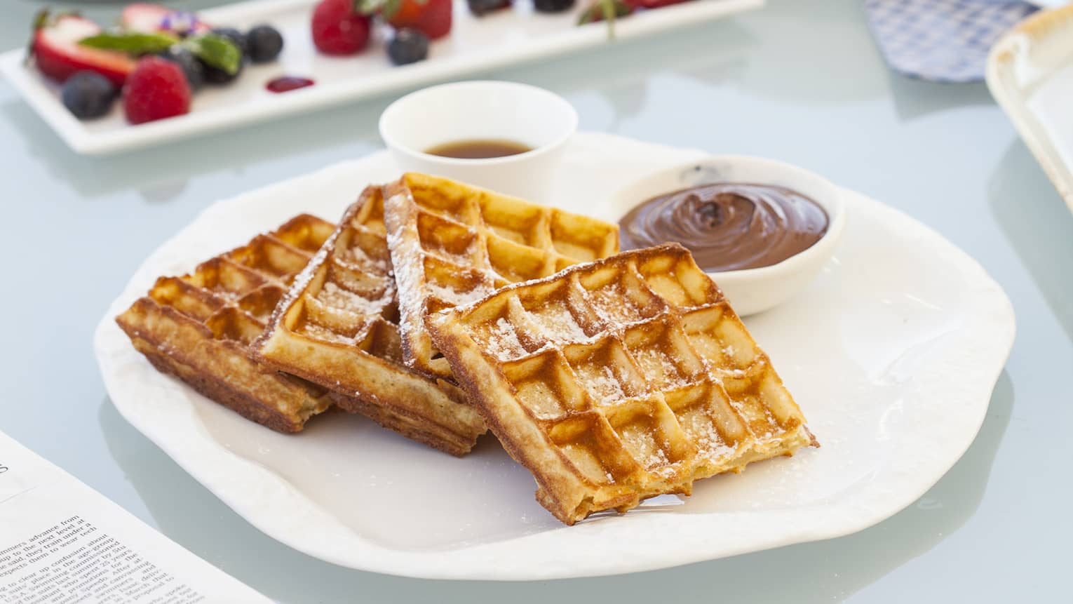 Breakfast table with coffee cup, three waffles, fruit on plate
