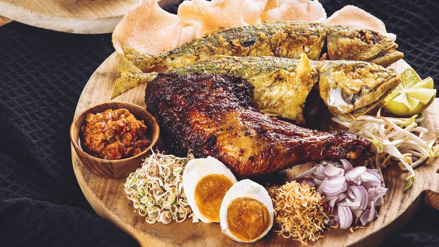 Traditional Malaysian spread with ayam percik chicken, whole fried fish, prawn crackers, rice cone trio and accompaniments
