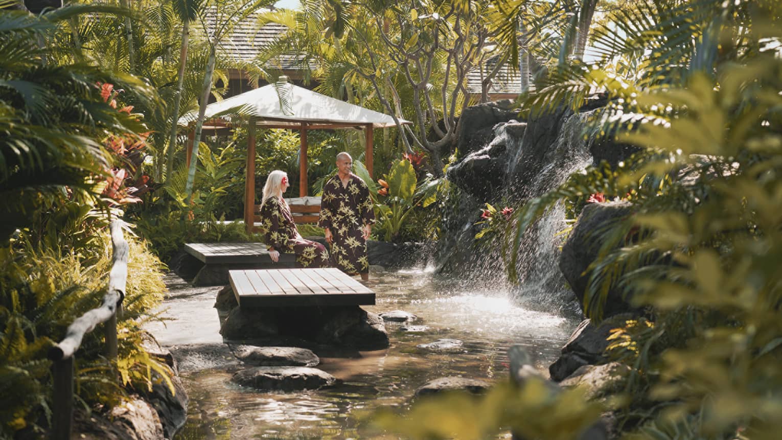 Two four seasons guests lounge in robes at the lush, vegetation-surrounded outdoor spa