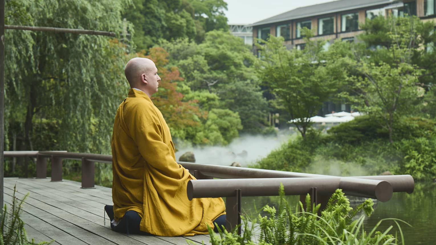 A monk sits at the edge of a serene pond