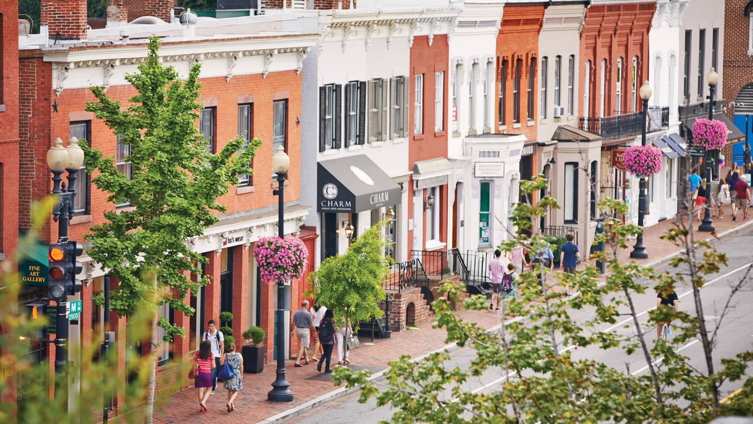View past trees over summer street where pedestrians walk by historic brick storefronts