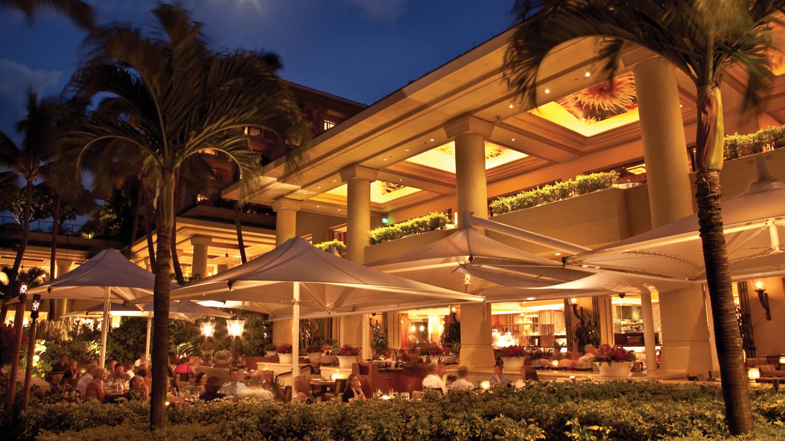Exterior of hotel and restaurant patio with umbrellas illuminated at night