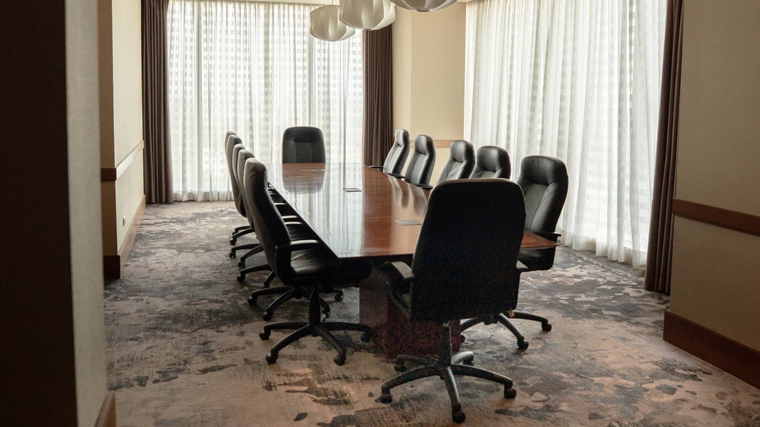 A softly lit meeting space with sheer drapes over large windows, and a long wood table with upholstered chairs in the centre of the space