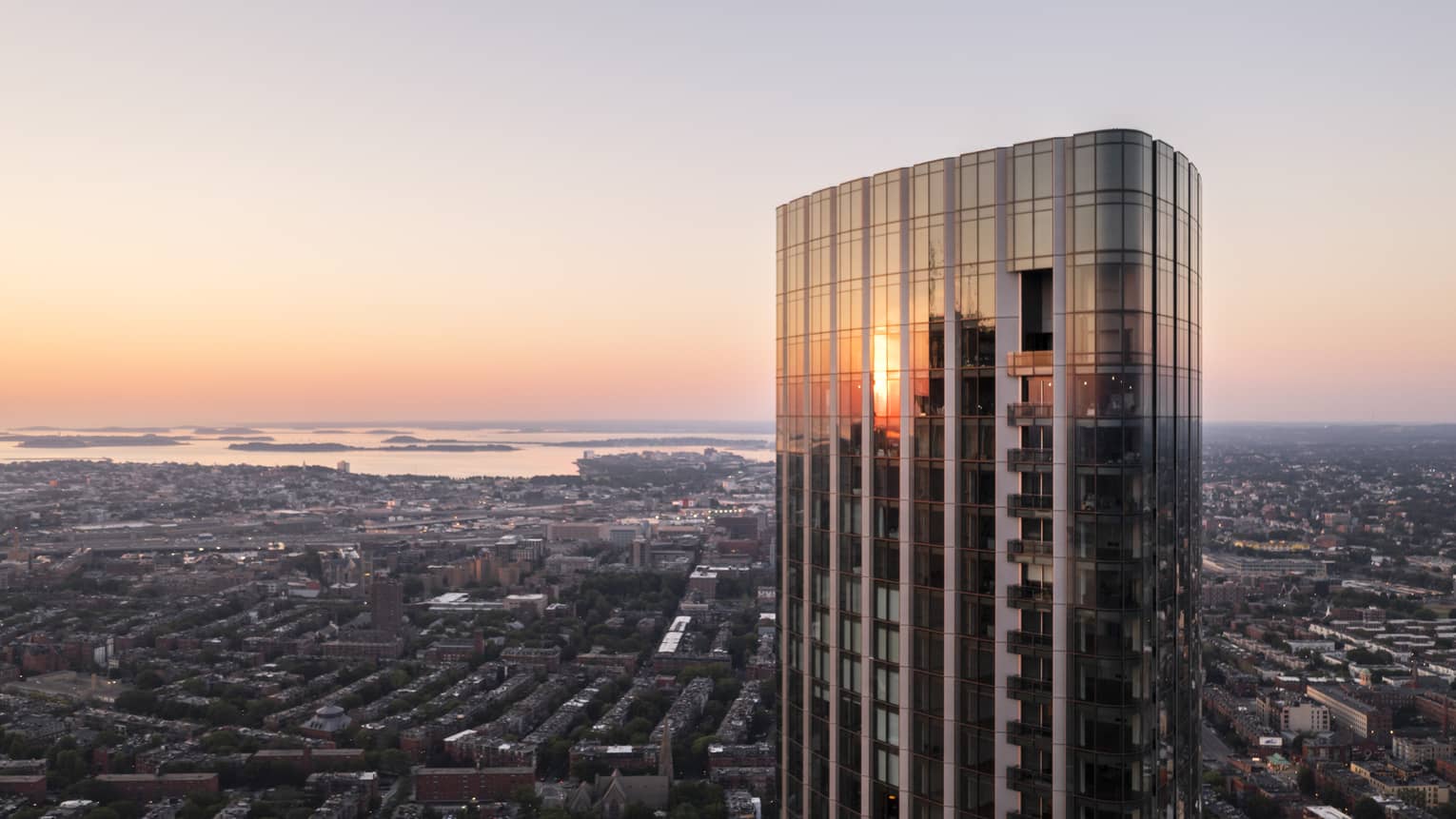 The exterior of a glass and steel skyscraper looking over a city with water in the distance.