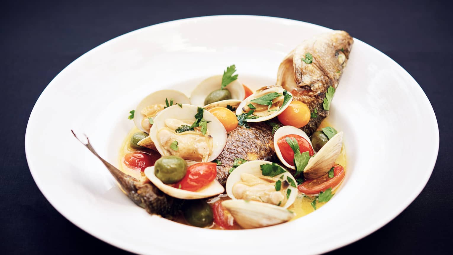 Whole fish with clams, shells, whole olives and tomatoes in bowl
