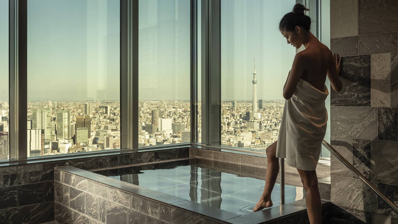 Woman wrapped in white towel dips her toe into the ofuro bath