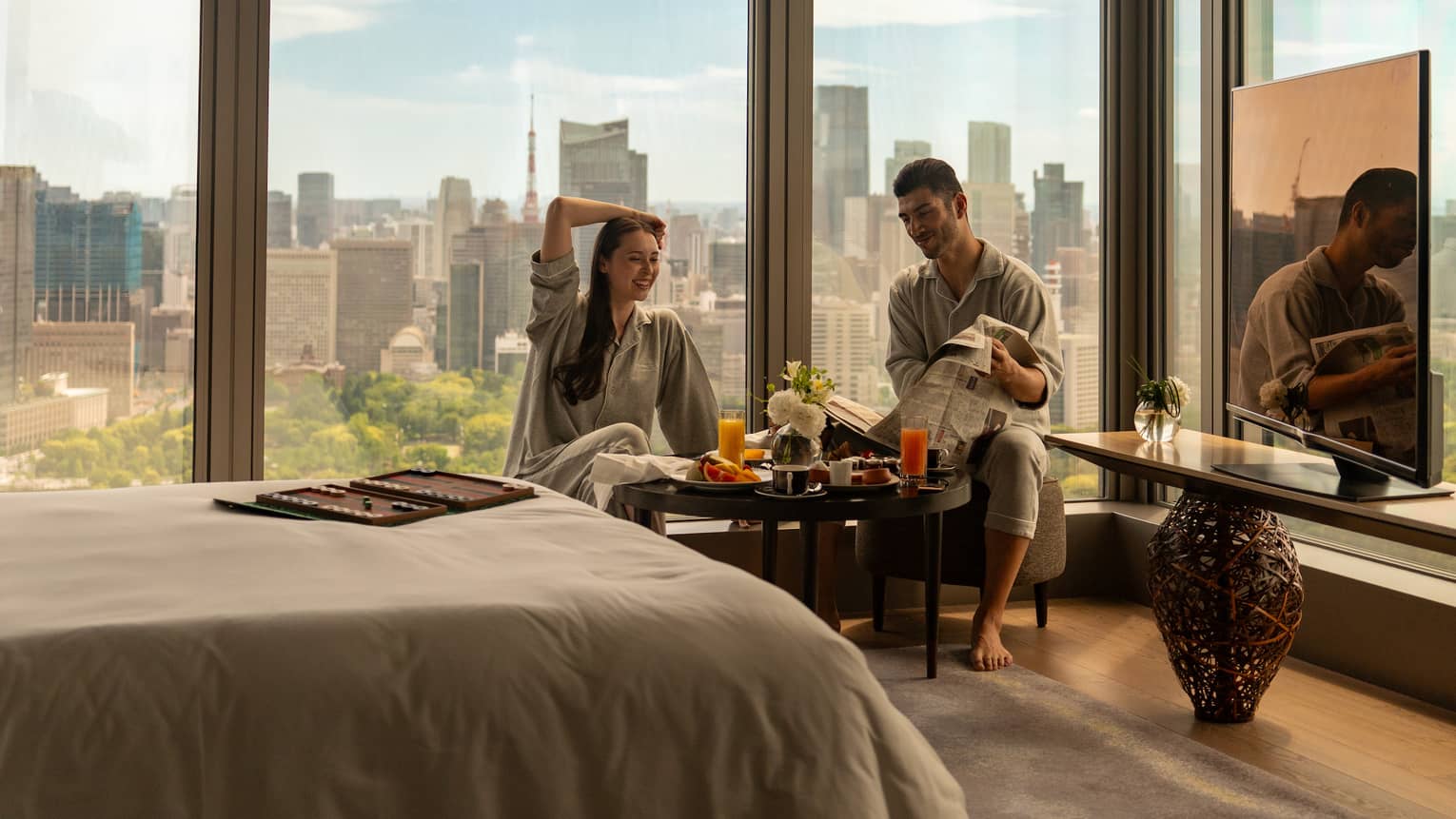 Two people enjoy breakfast in their hotel room with city skyline out their window