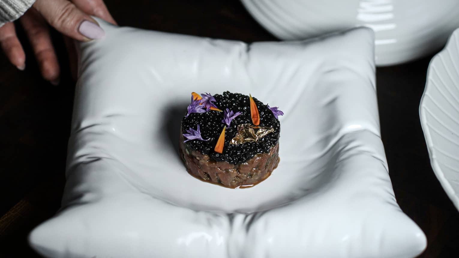 Hand placing a round white bowl of food onto a dark table with a dark backdrop