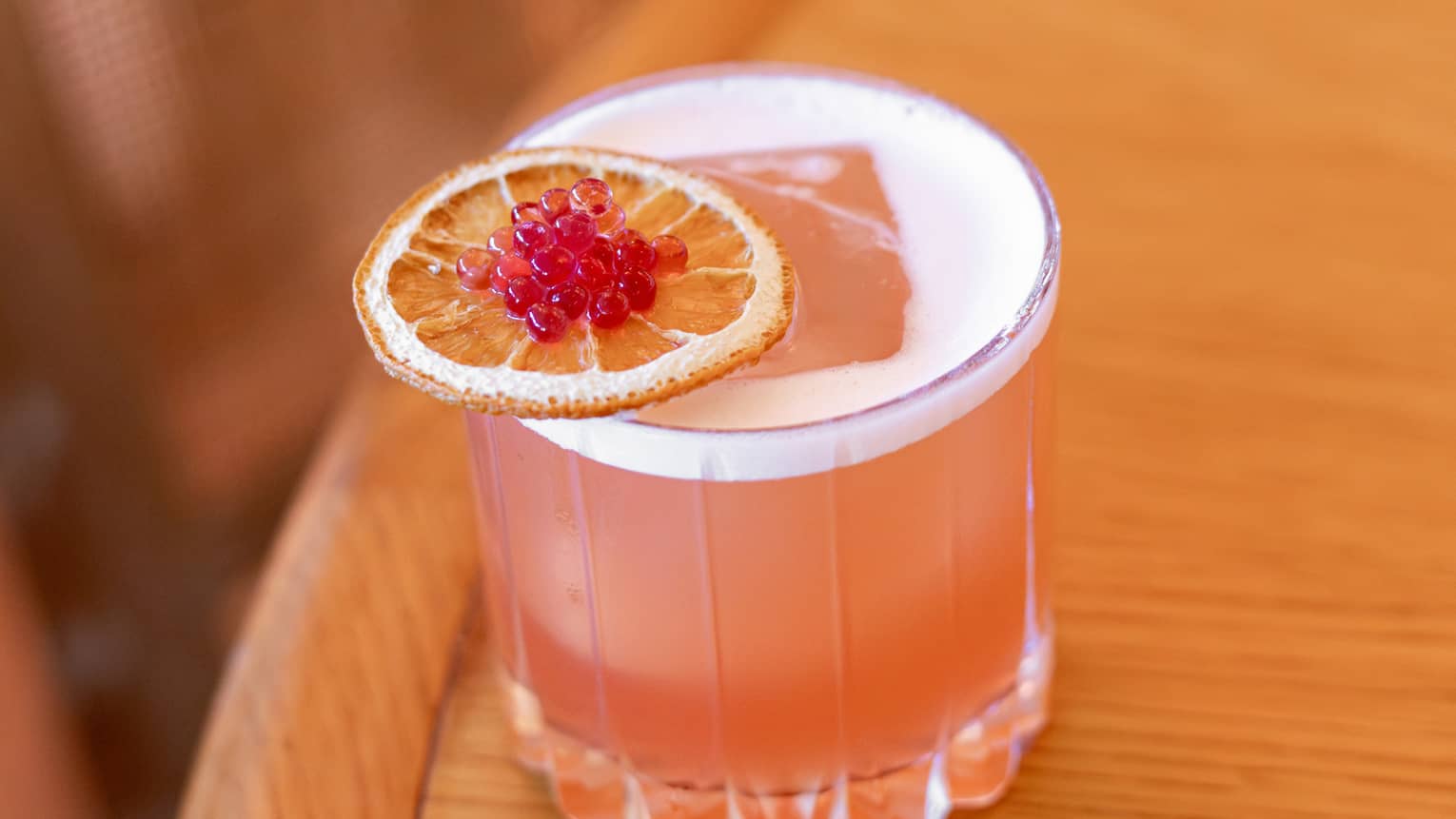 Coral-hued cocktail served in a rocks glass and garnished with an orange slice