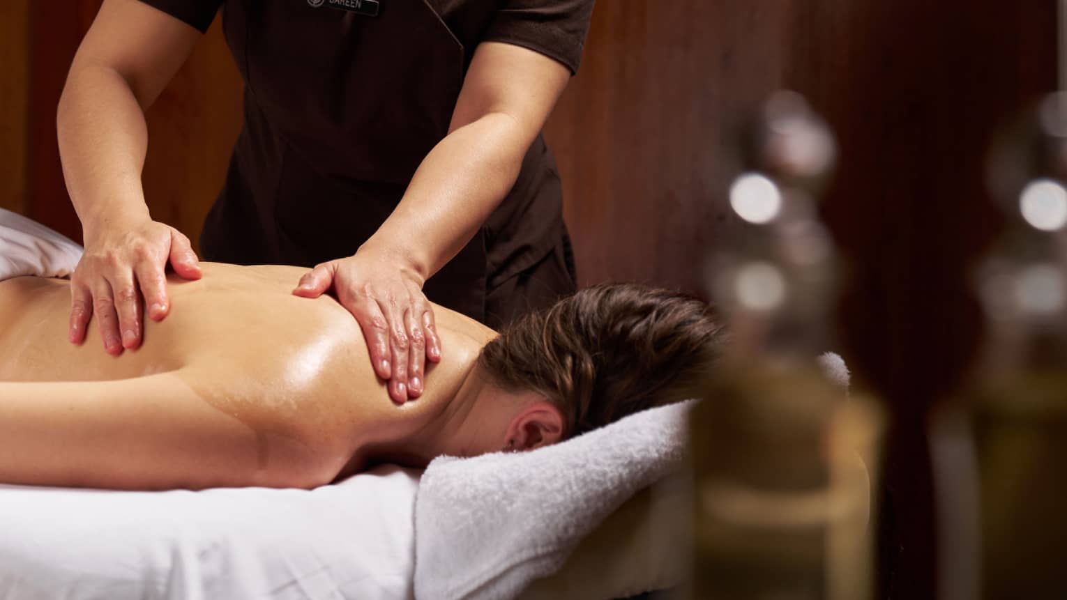 Masseuse performs treatment on female guest lying face down on massage table
