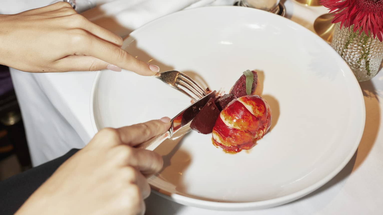 Two people sit at white-cloth table, cutting into contemporary dish on large white plate