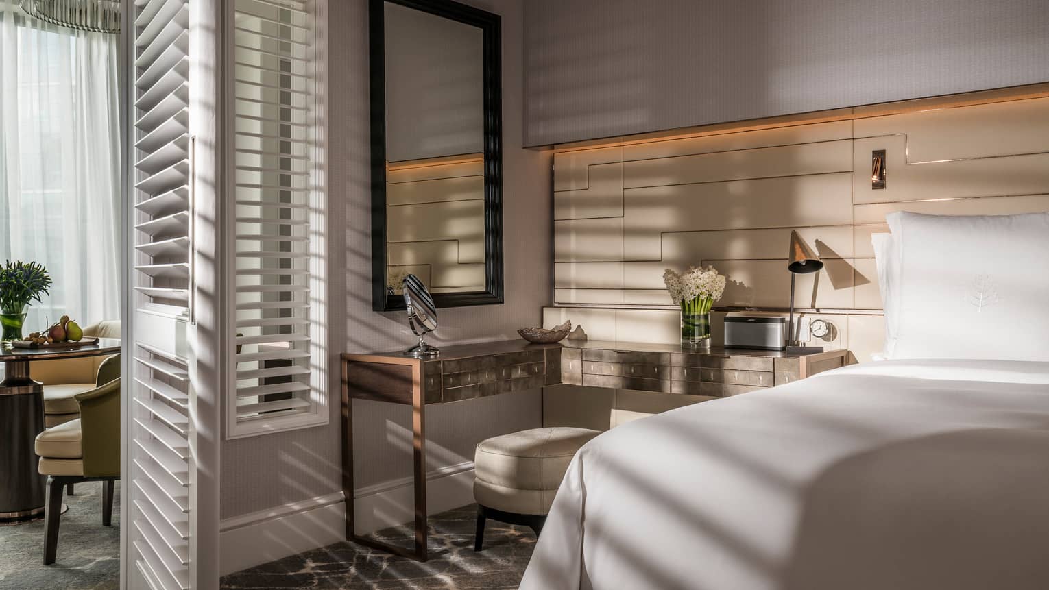 Sun streams into bedroom through tall white California shutters on dining room wall