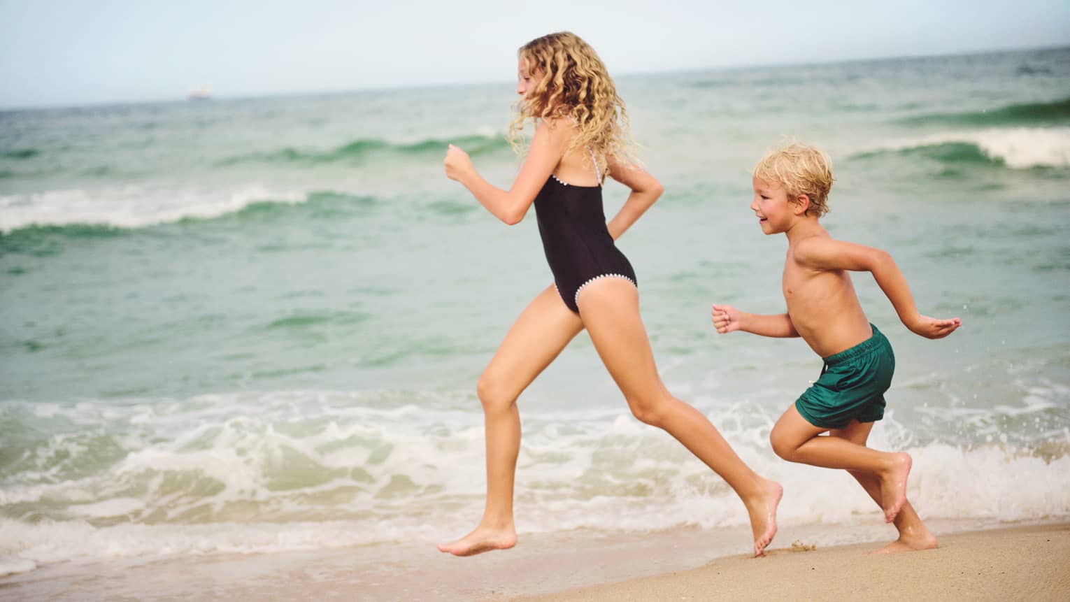 Two children run along the beach by the waterline