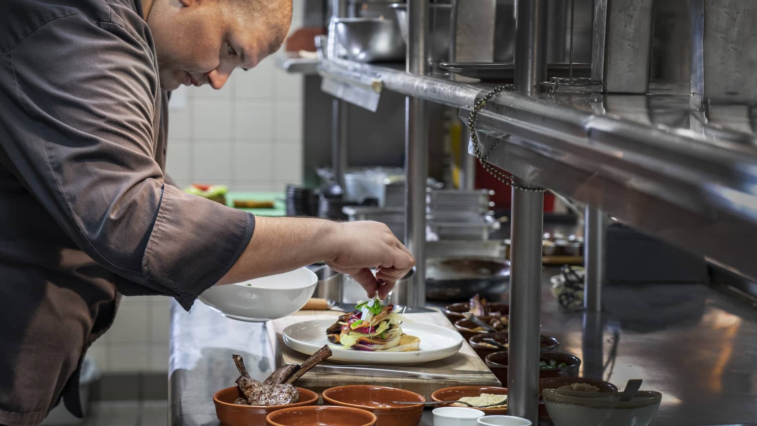 Chef garnishes gourmet meat entree on steel kitchen line