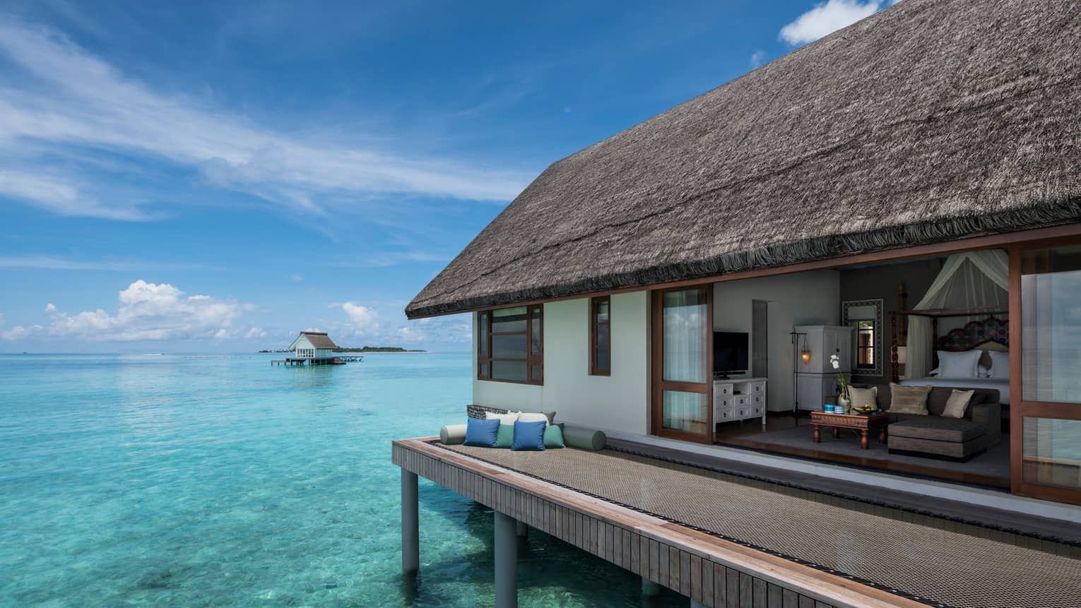 Overwater bungalow with thatched roof, set atop clear turquoise water