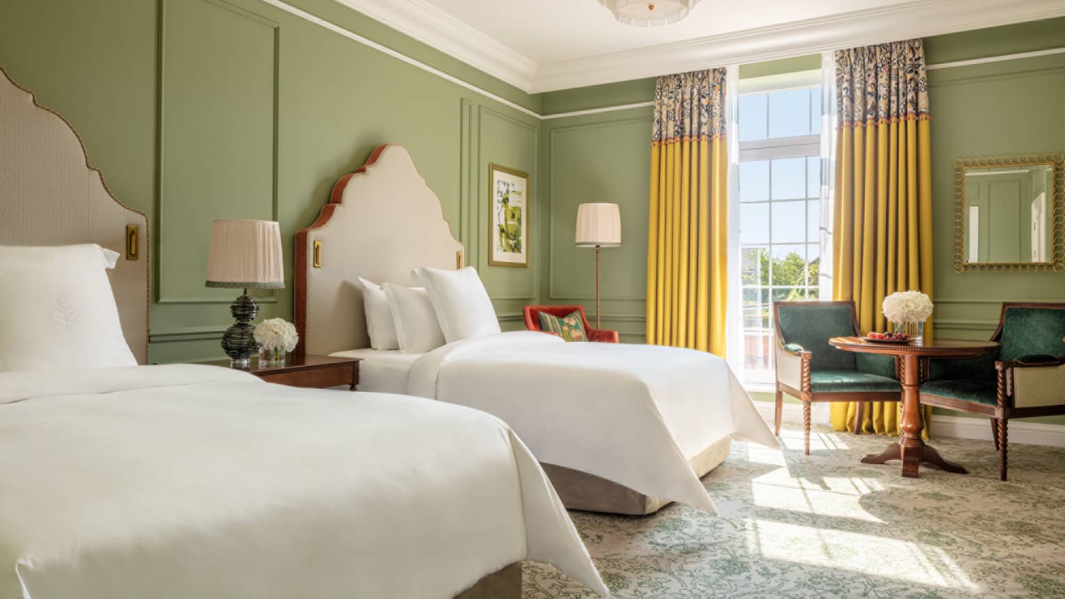 Mews Room with two queen beds, paisley carpeting, avocado-coloured walls, accent table with two chairs, floor-to-ceiling window with yellow drapes
