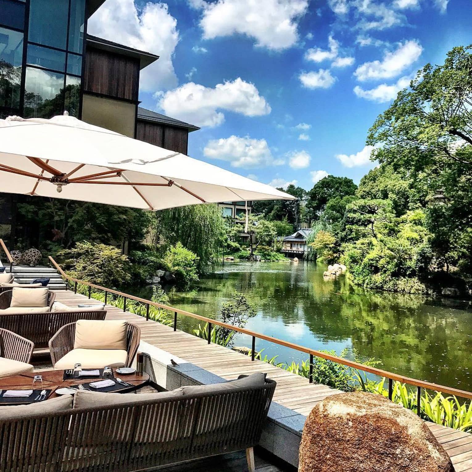 Outdoor seating area with parasols overlooking a peaceful garden pond at Four Seasons on a sunny day