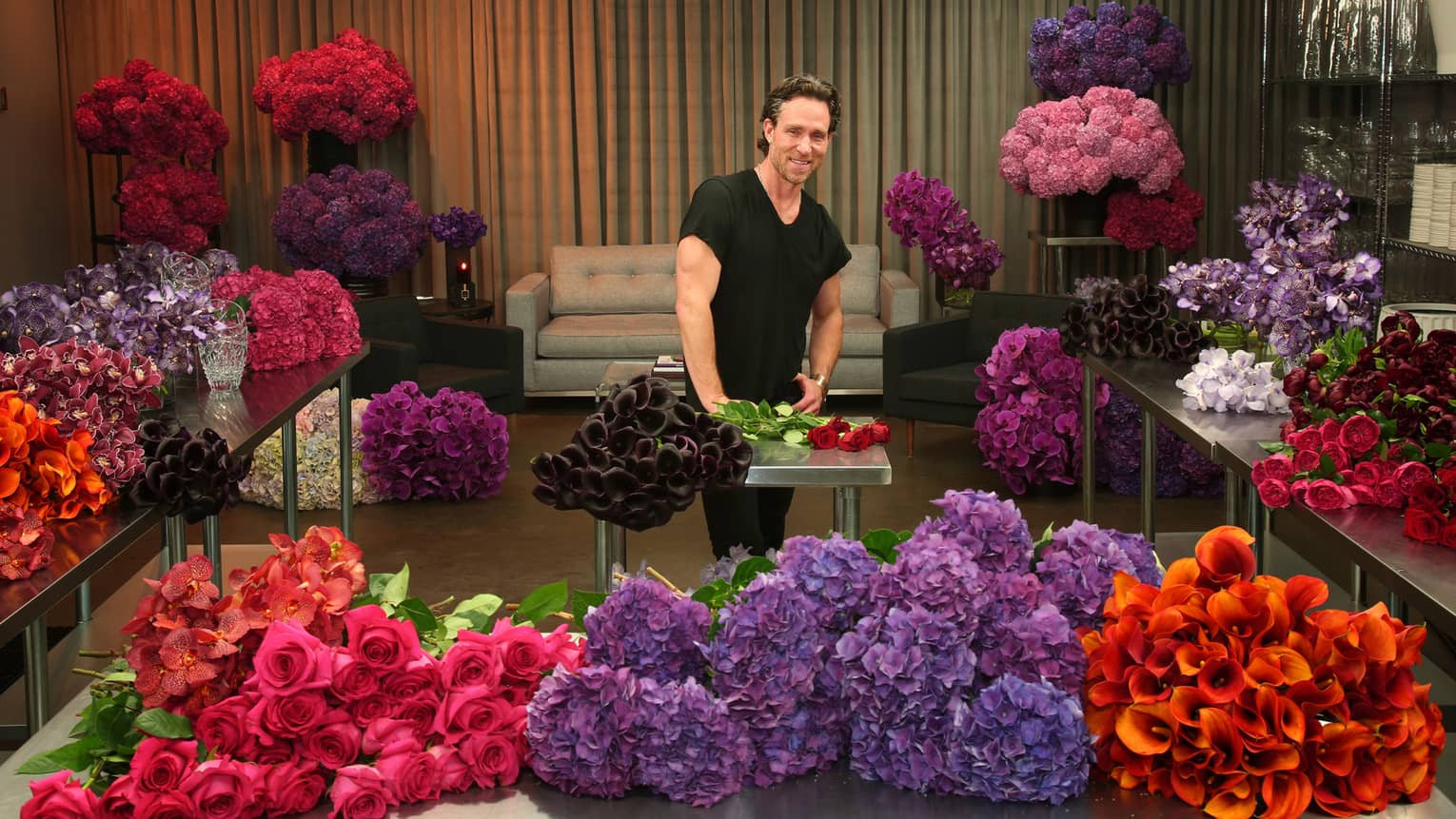 Florist Jeff Leatham stands at table surrounded by piles of colourful flower bouquets
