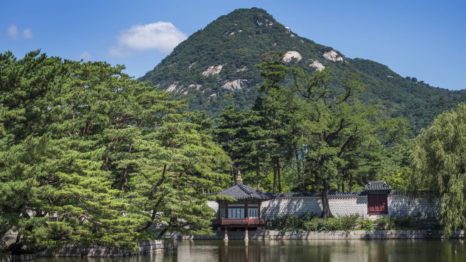 Temple surrounded by water with lush, green mountain in background and green trees