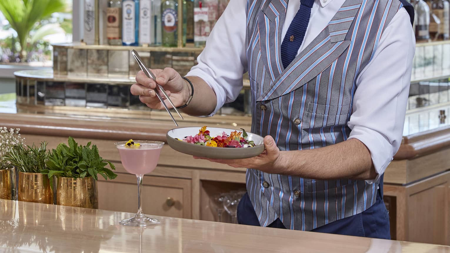 Mixologist holds tray with edible flowers, garnishes cocktail