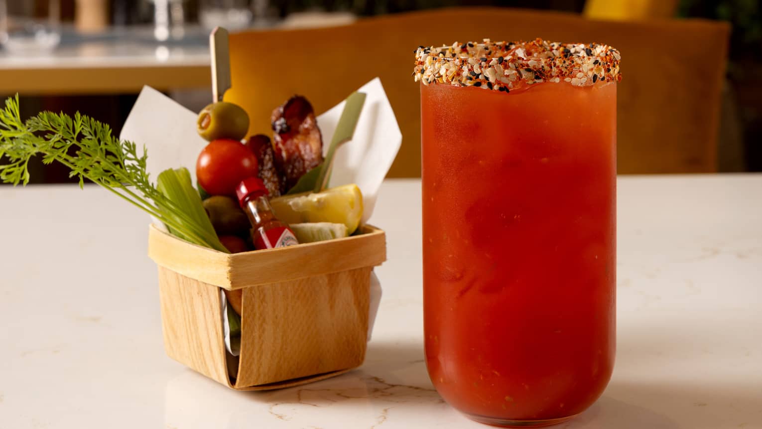 A Bloody Mary cocktail served in a clear glass beside a small basket of garnishes.
