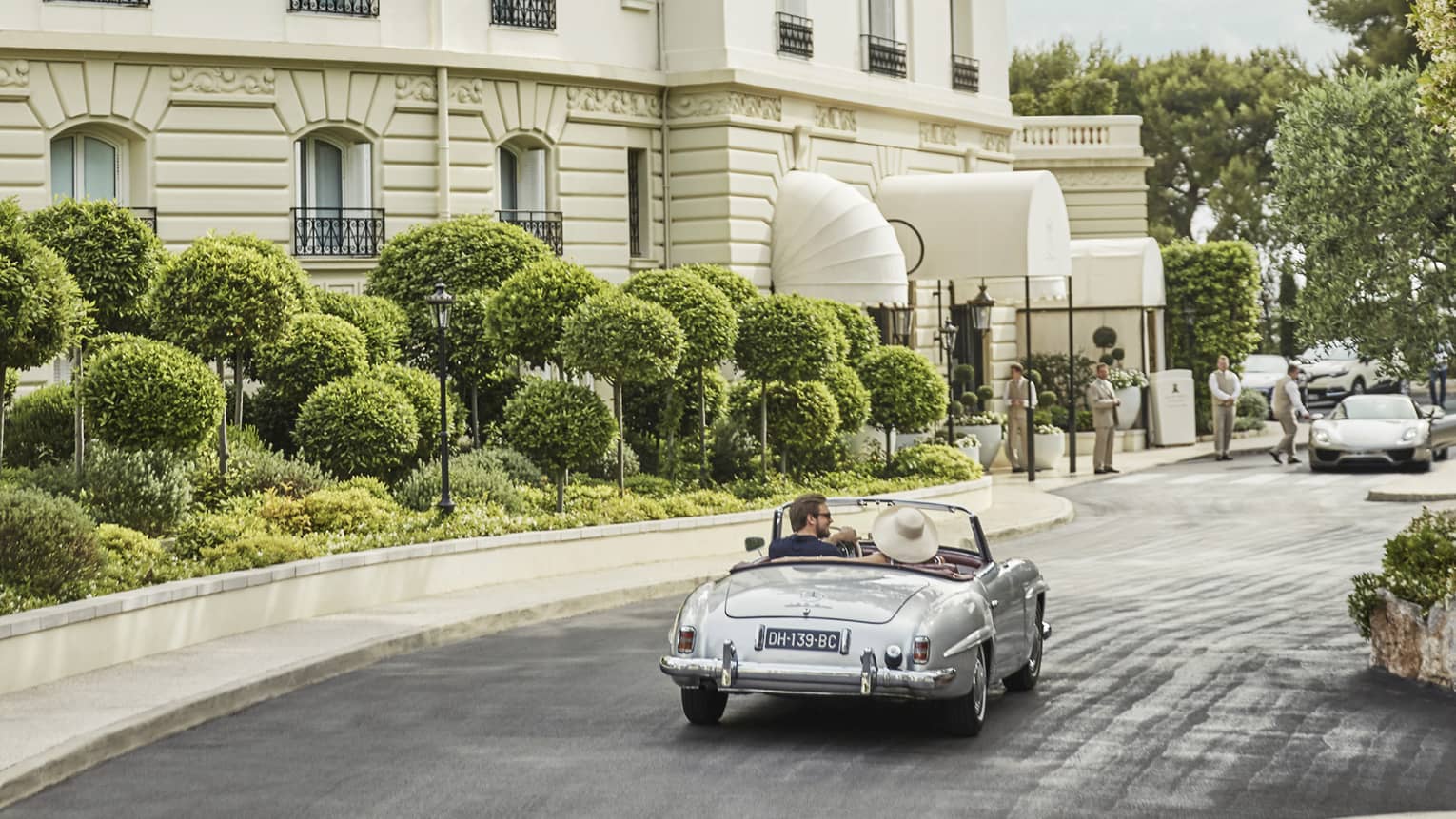 Back view of couple driving luxury convertible bar along sunny city road