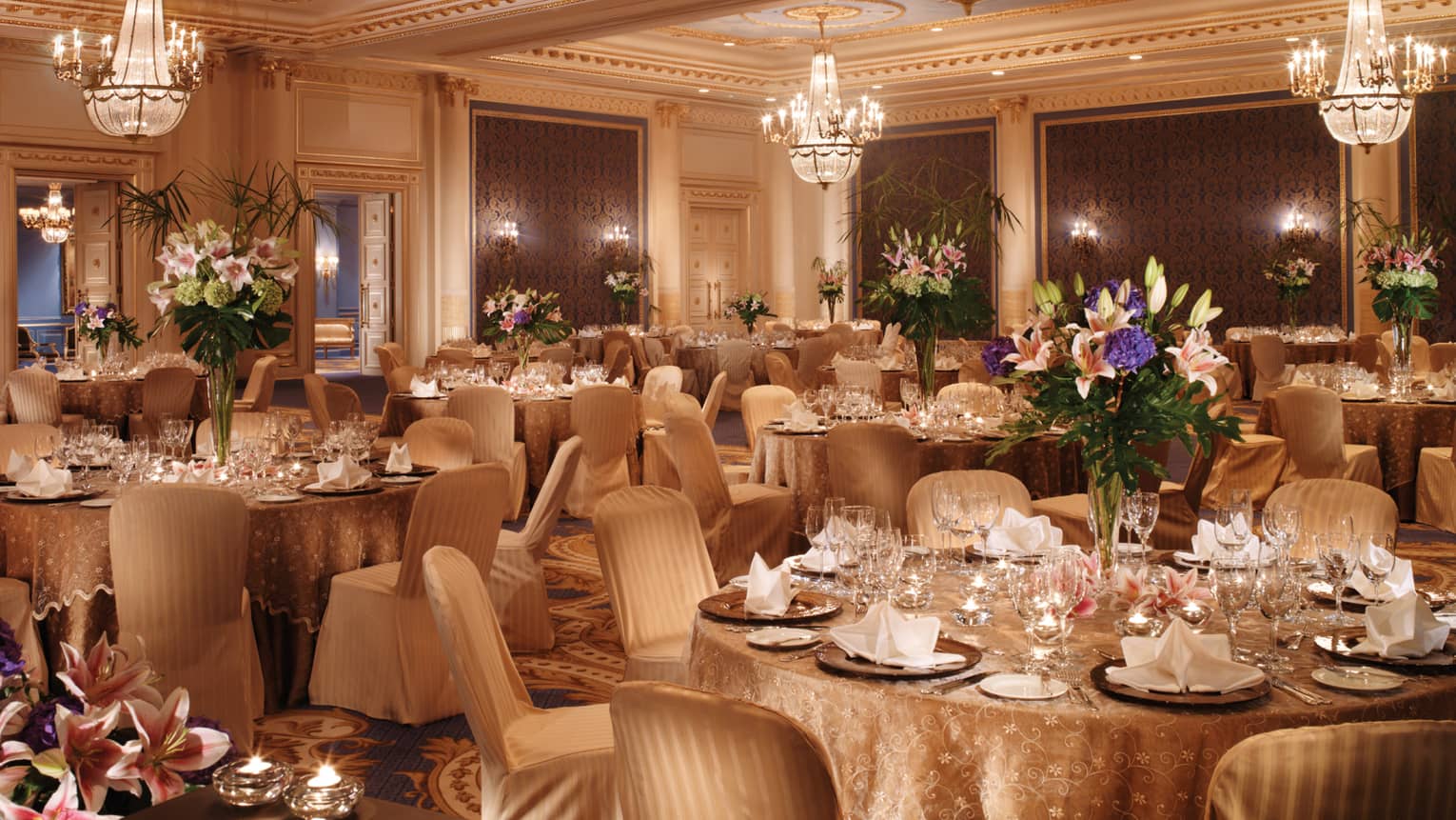 Elegantly set tables with gold tablecloths, flowers in ballroom with textured blue panels chandeliers 