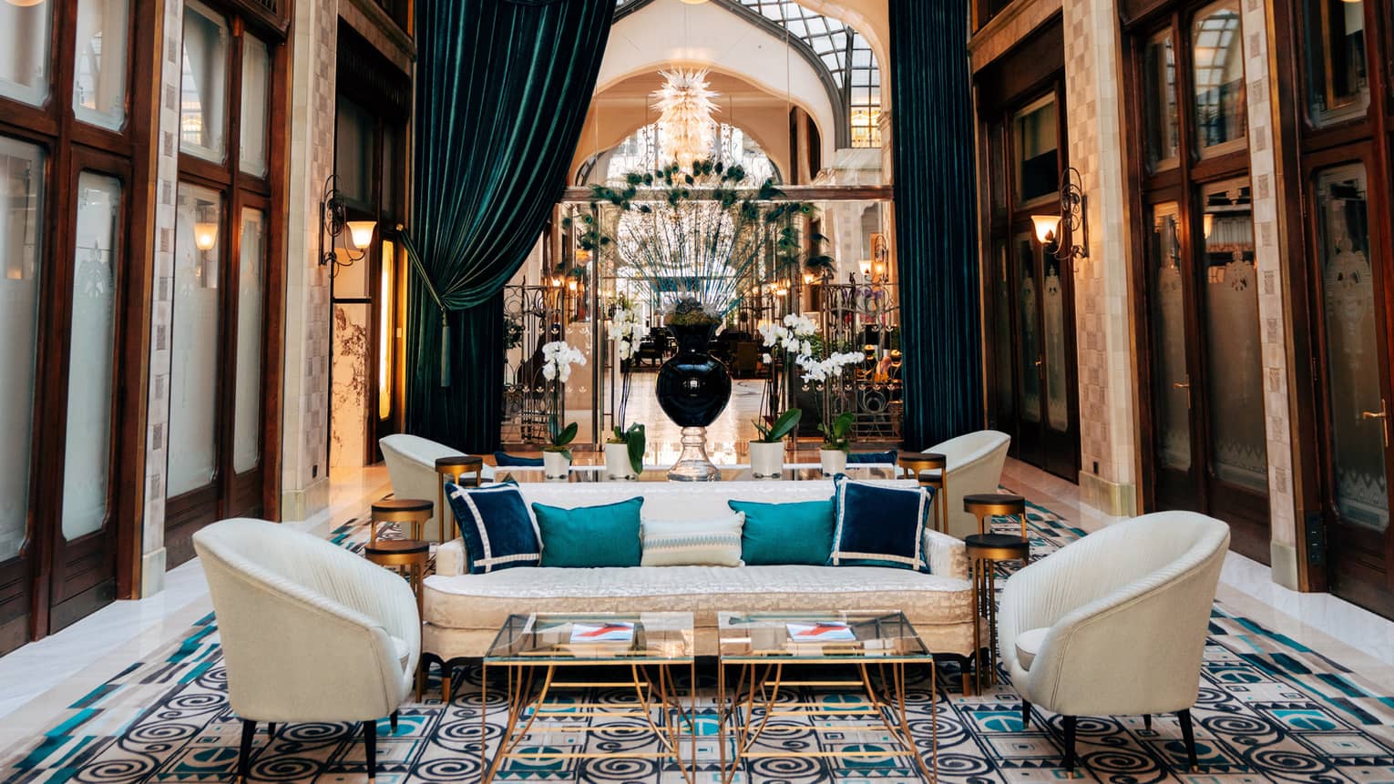 Zrínyi Passage with Zsolnay tiles, white chairs and couch, blue cushions, drapes and high ceiling